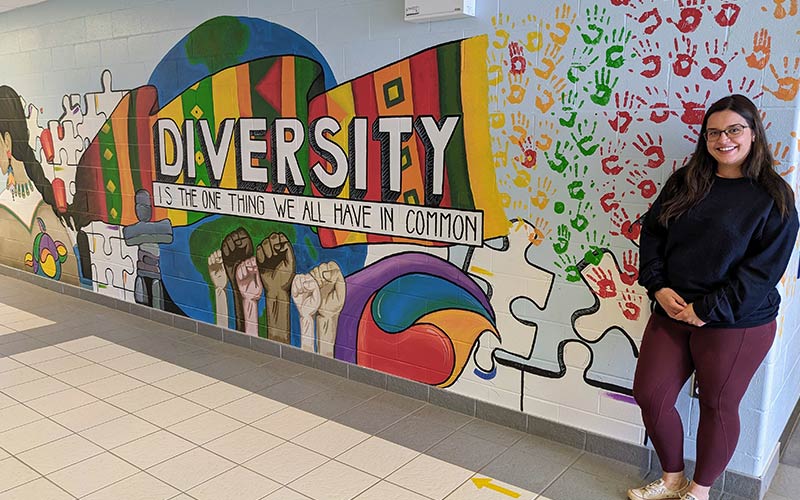 KENT Building Supplies associate stands before a mural featuring the word 'diversity,' promoting inclusivity and community.