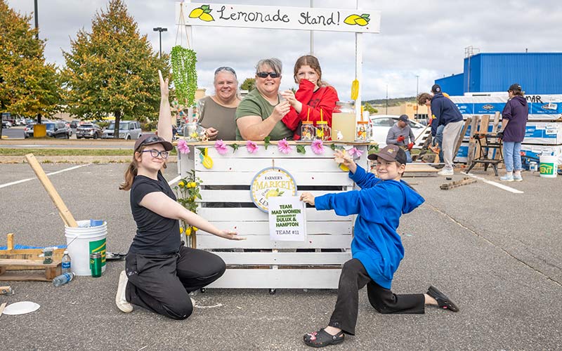 KENT Building Supplies associate and family members pose beside a lemonade stand during a lively community gathering.