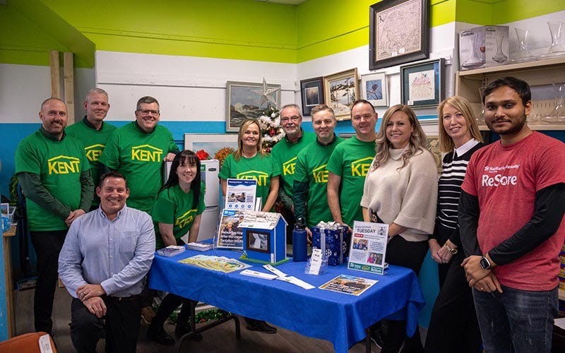 Several KENT associates in green shirts standing together around a table, participating in a charity discussion